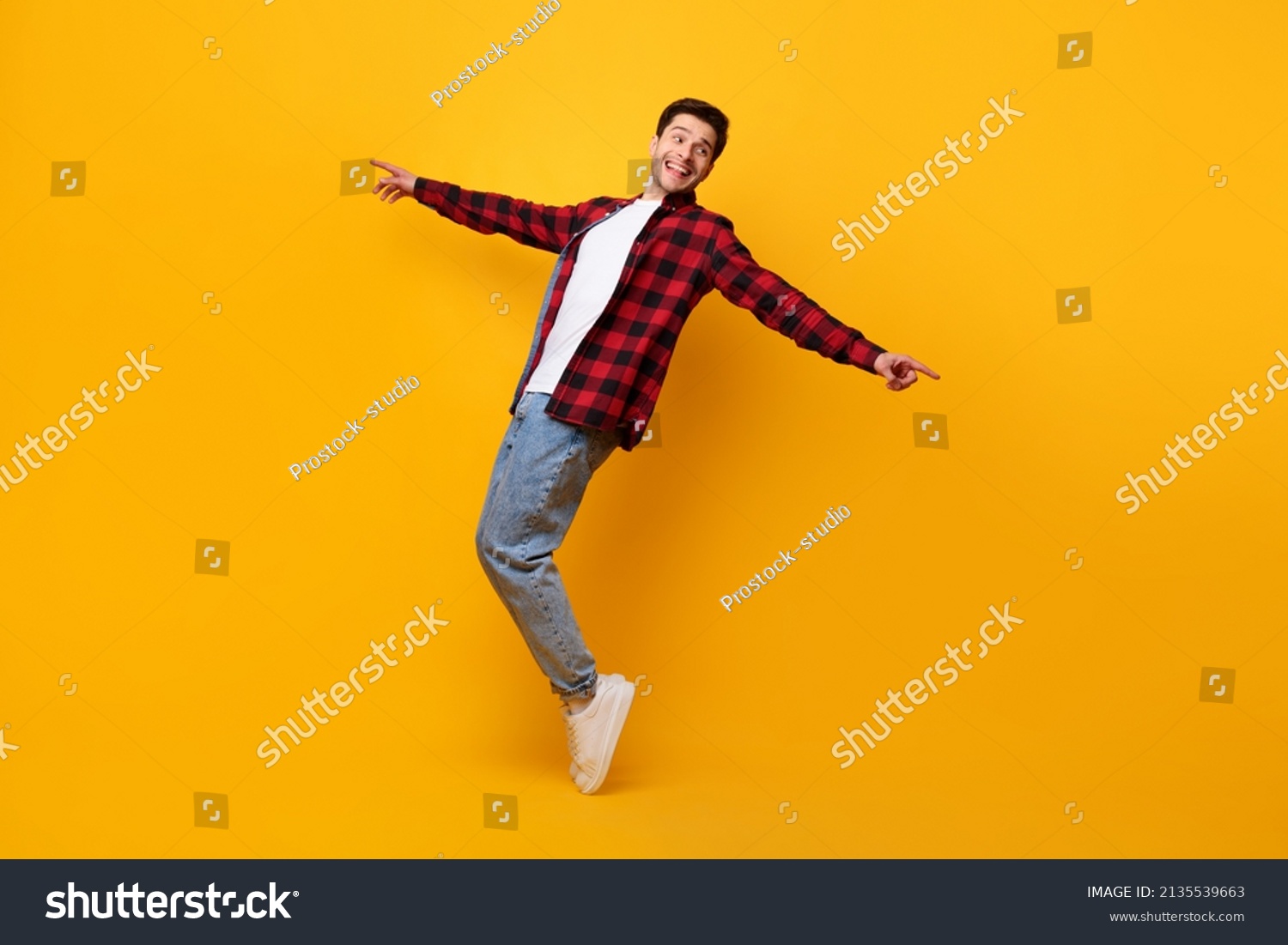Happy excited funny man dancing to favorite song standing on tiptoes isolated over yellow orange studio background wall, pointing at copy space. Male doing disco moves enjoying sound and music, banner #2135539663