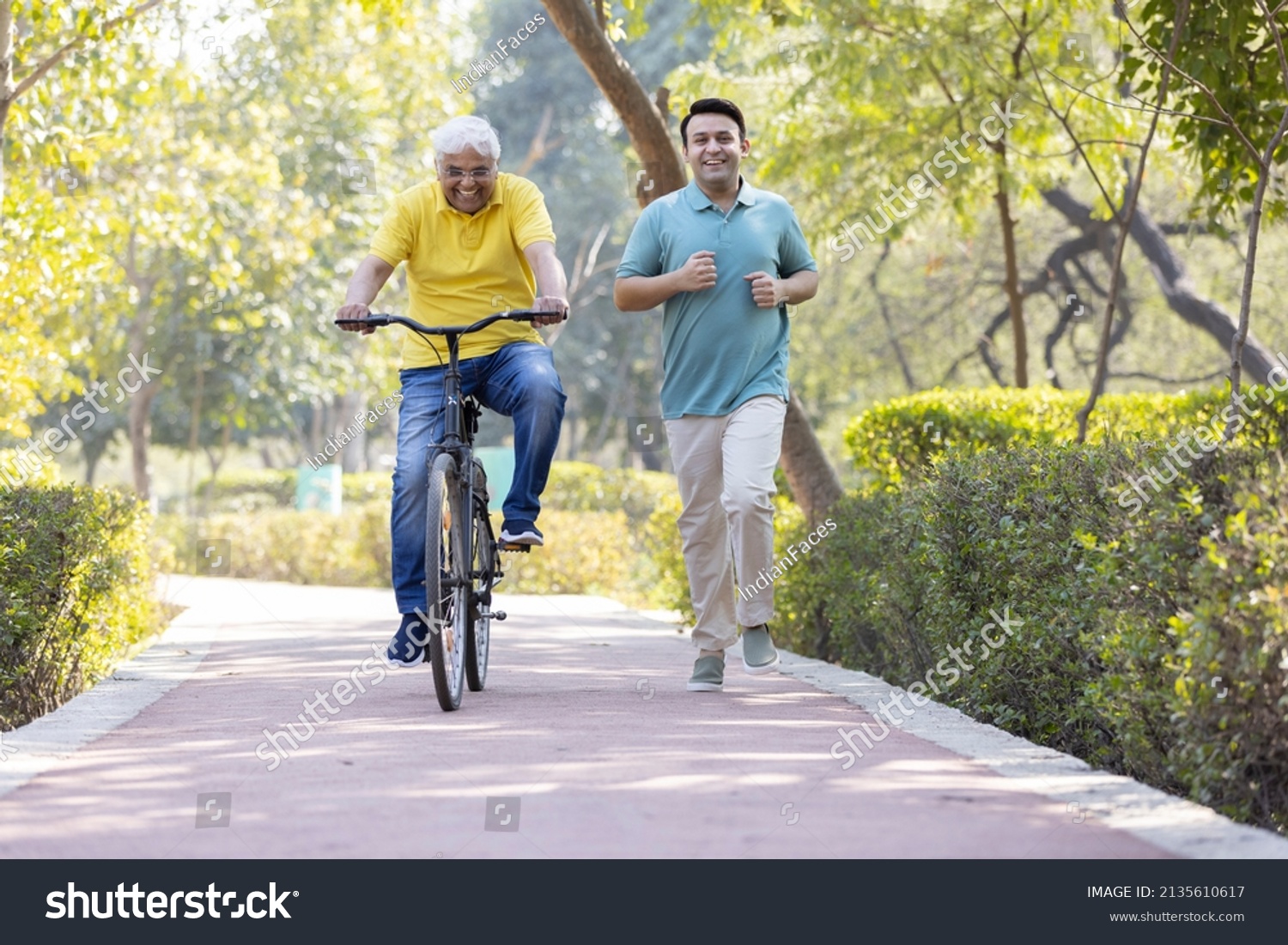 Cheerful senior man riding bicycle  while son running at park
 #2135610617