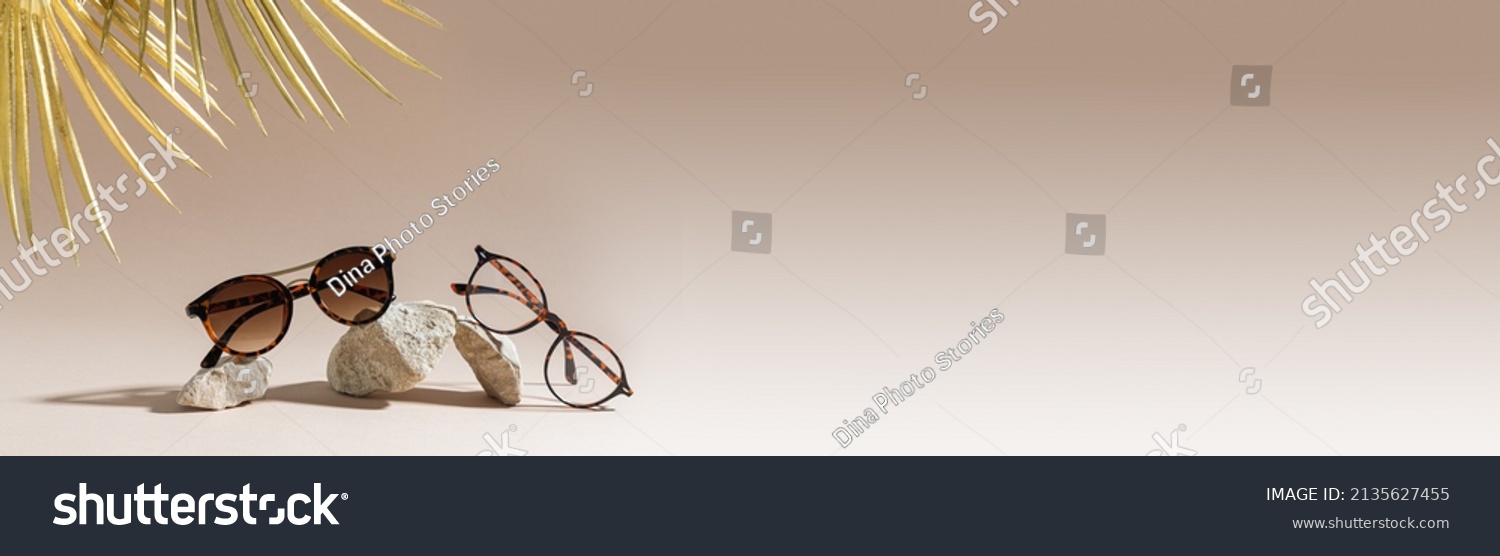 Optic store advertisement banner. Clear Eyeglasses Glasses with plastic Frame and trendy sunglasses on a beige Background. Tortoiseshell frame glasses on stones. Copy space. Optic store web line #2135627455