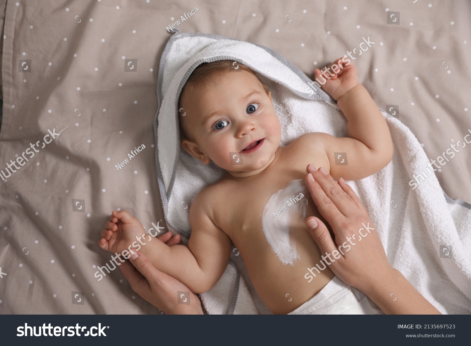Mother applying moisturizing cream onto her little baby's skin on bed, closeup #2135697523
