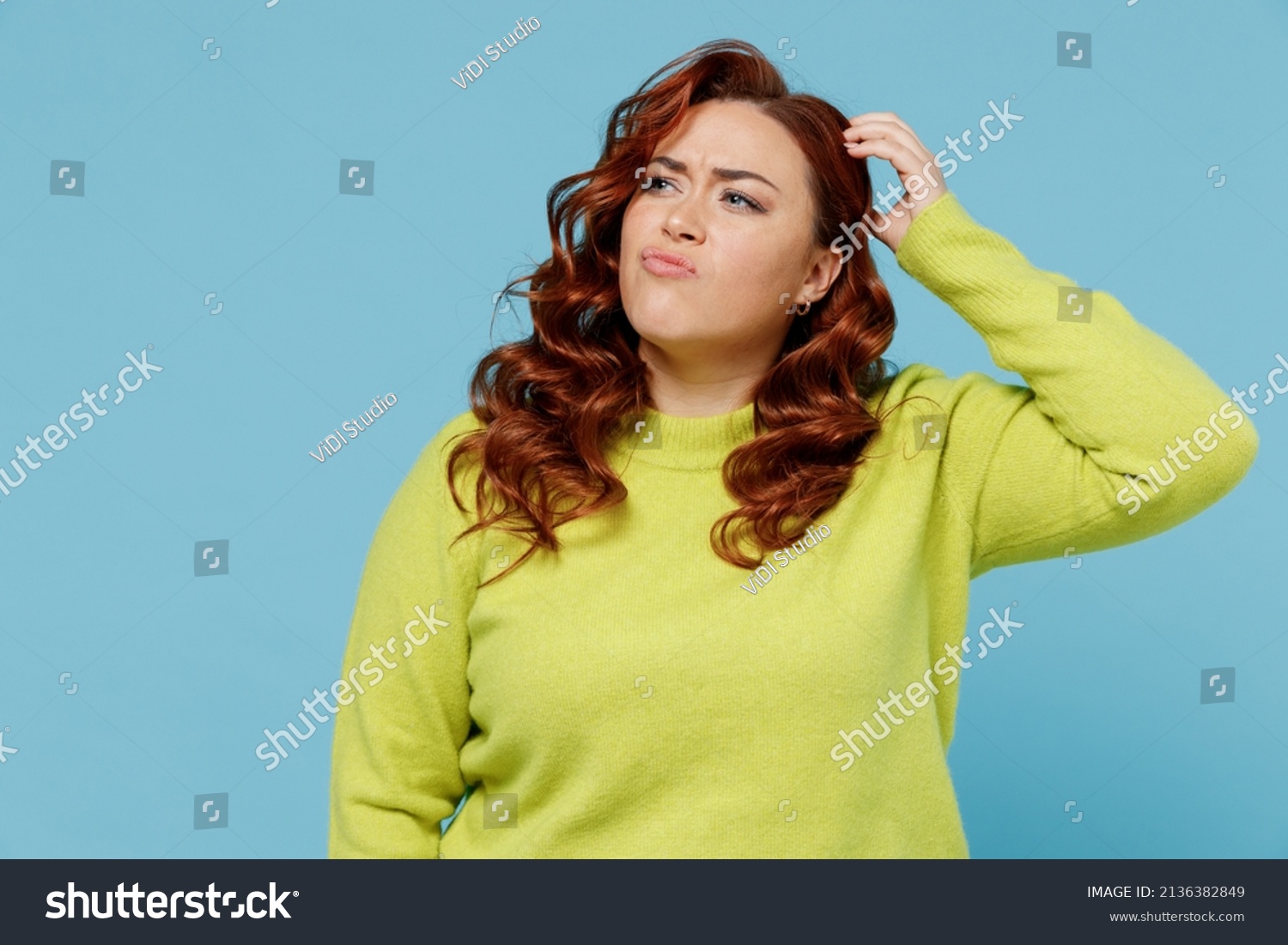 Young puzzled thoughtful confused chubby overweight plus size big fat fit woman wear green sweater look aside scratch head isolated on plain blue background studio portrait. People lifestyle concept #2136382849