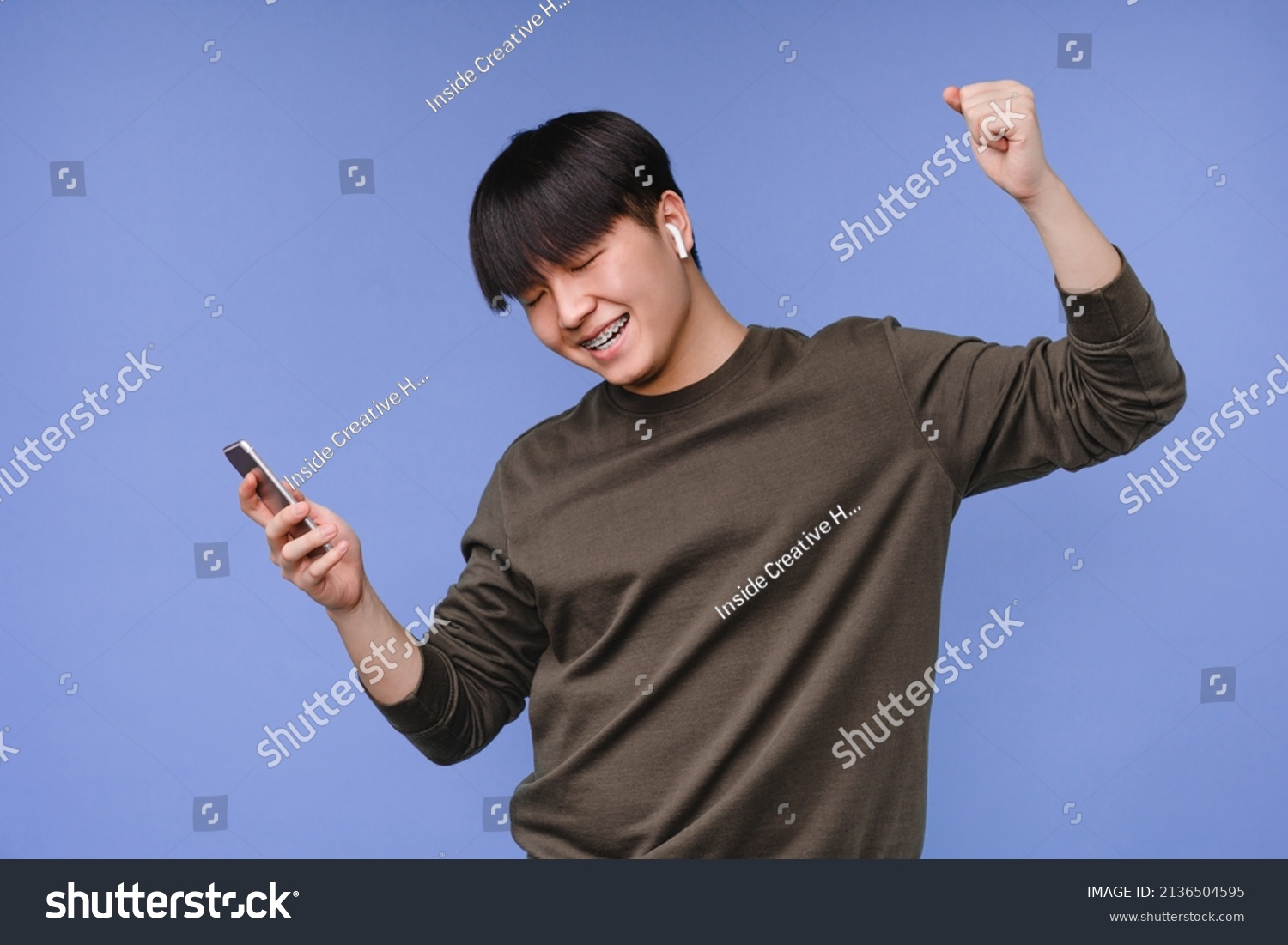 Dancing active asian korean young man boy student listening to the music on cellphone using earbuds, choosing soundtrack, playlist, radio isolated in blue background #2136504595