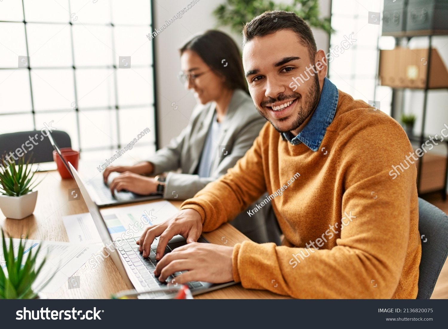 Two business workers smiling happy working sitting on desk at the office. #2136820075
