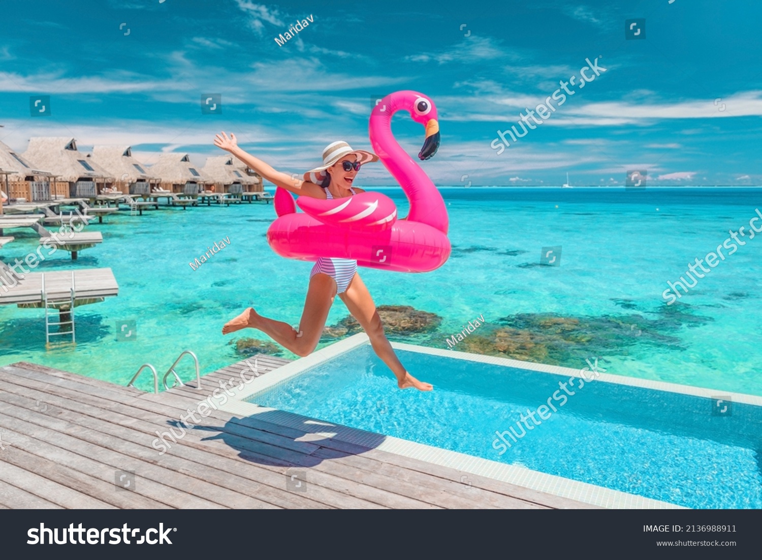 Luxury hotel beach vacation ocean overwater bungalows suite resort. Happy woman tourist jumping of joy in funny pool toy flamingo float excited to be in Bora Bora resort, French Polynesia. #2136988911