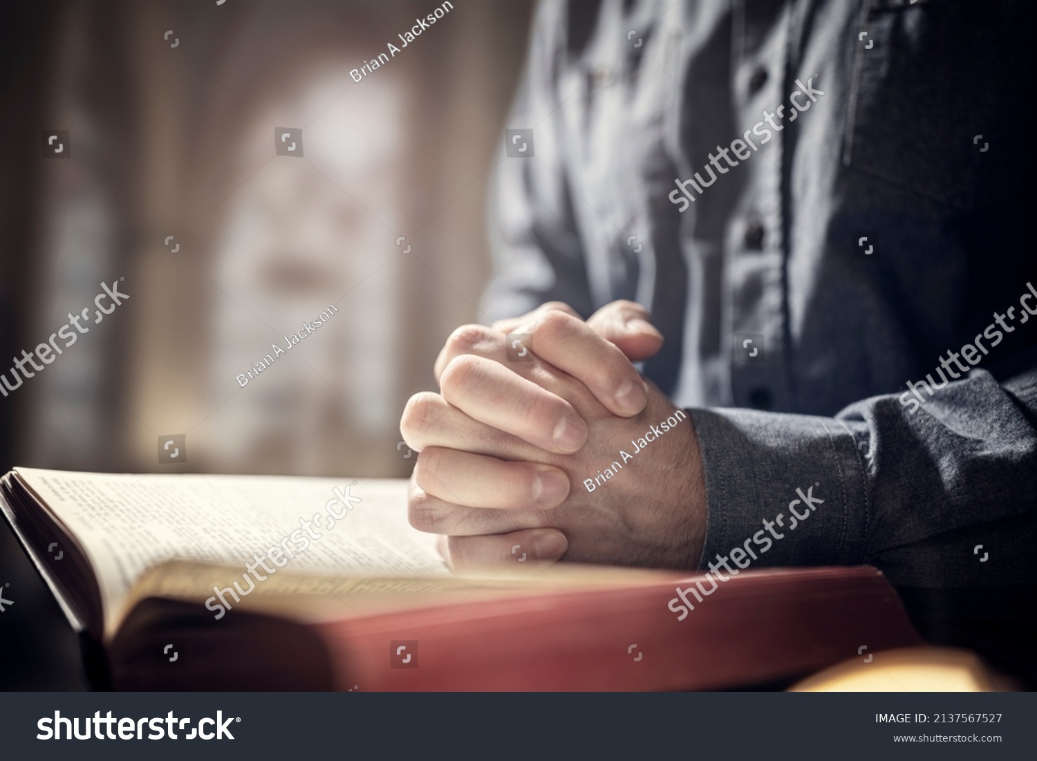 Hands folded in prayer on a Holy Bible in church concept for faith, spirtuality and religion #2137567527