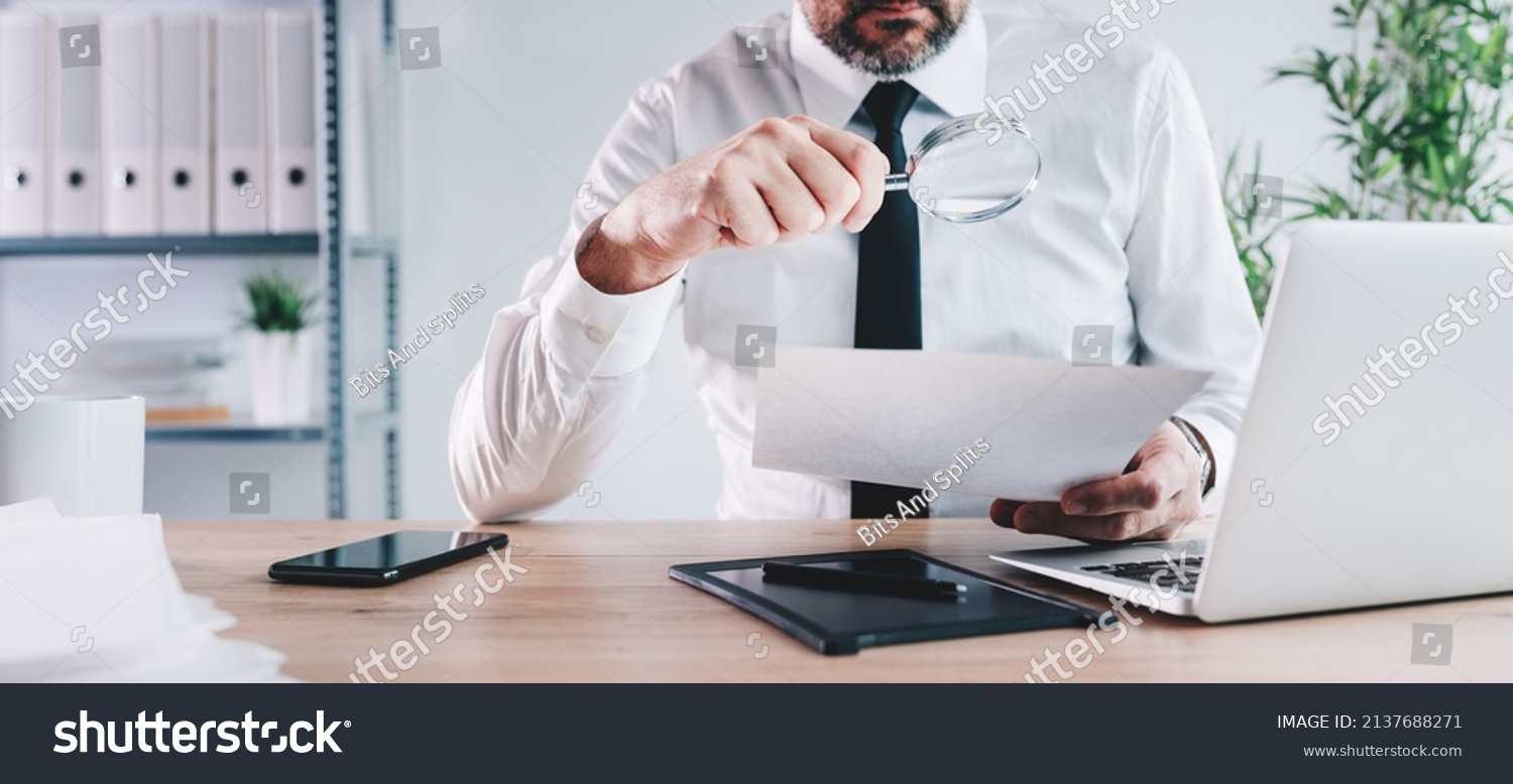 Tax inspector and financial auditor looking through magnifying glass, inspecting company financial papers, documents and reports, selective focus #2137688271