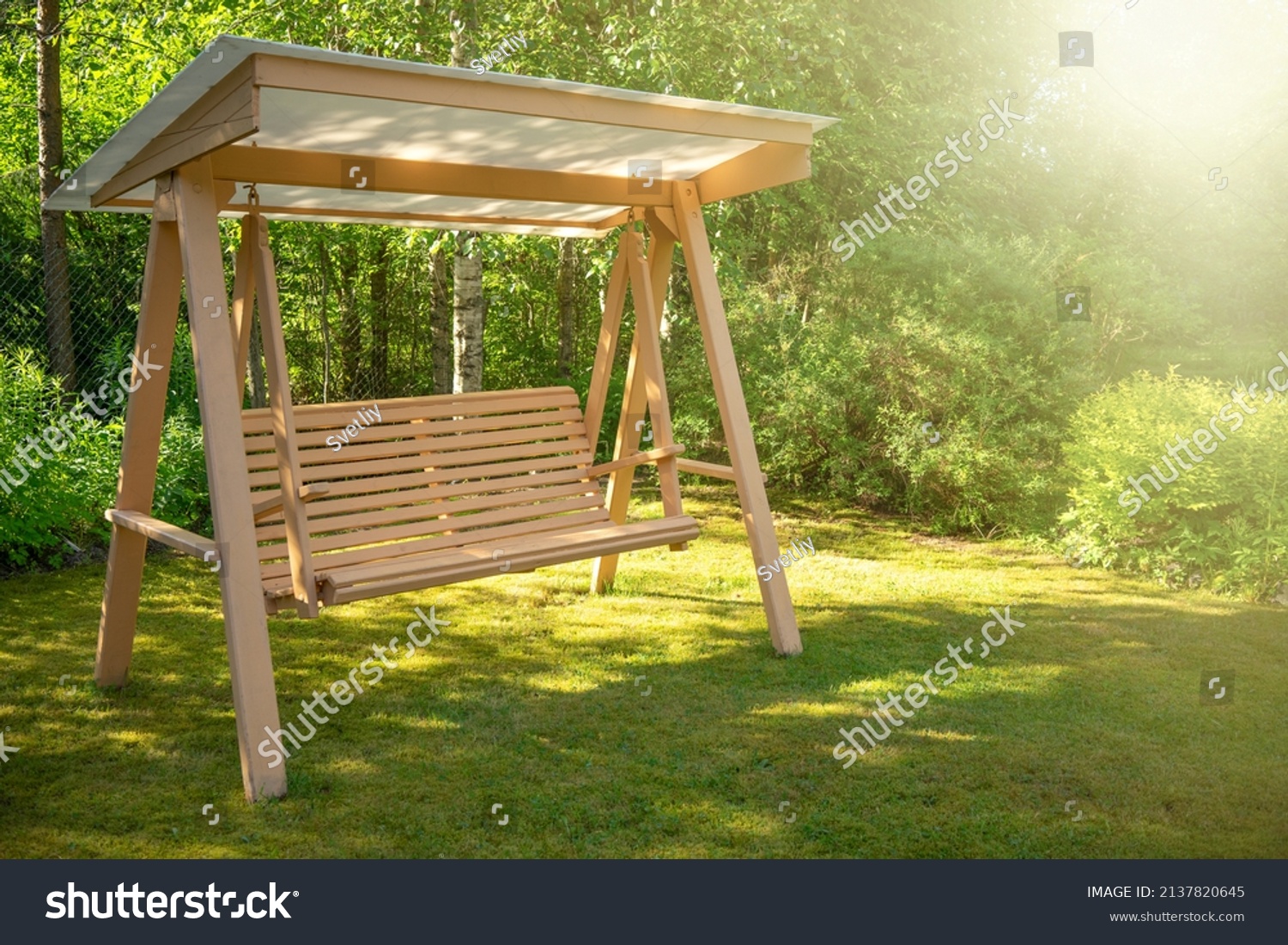 Wooden swing in the green garden. Landscaping of a private plot for recreation. Vacation in the country in summer. Swing for the garden with your own hands. #2137820645