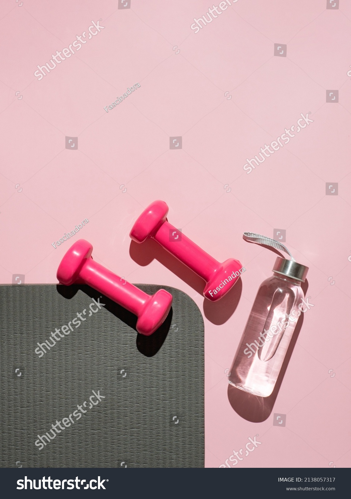 Stylish gray, water bottle and pink fitness training and gym flat lay. Top view of gray sport mat and pink dumbbells on pink background. Set for pilates, fitness with copy space. Vetical #2138057317