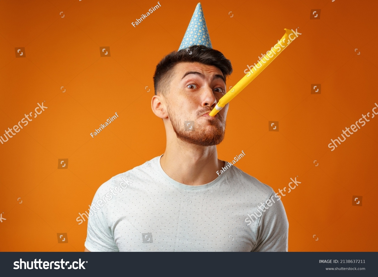 Happy man with party cone blowing into party horn #2138637211