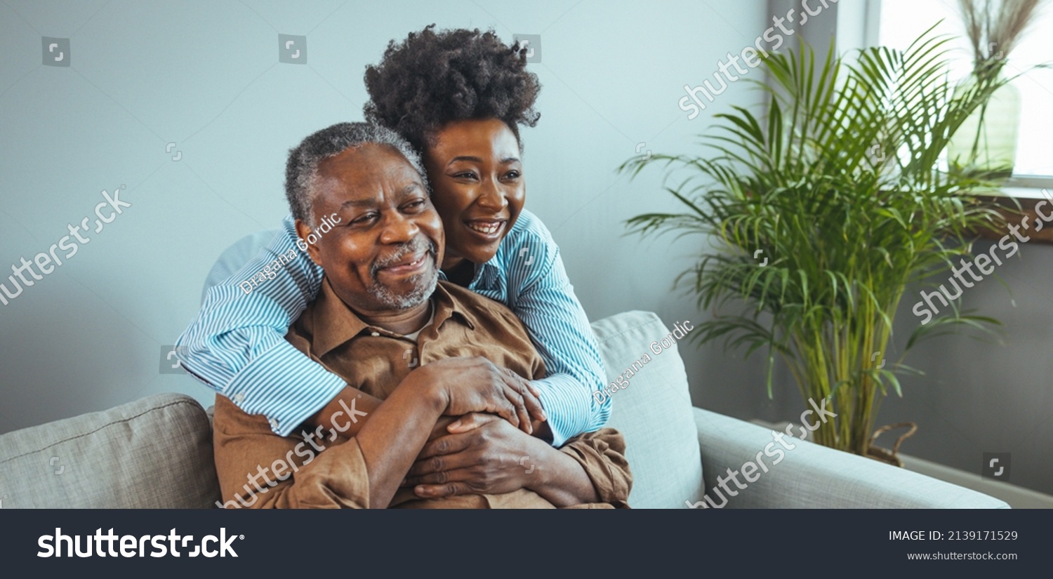 Adult daughter visits senior father in assisted living home. Portrait of a daughter holding her elderly father, sitting on a bed by a window in her father's room.  #2139171529
