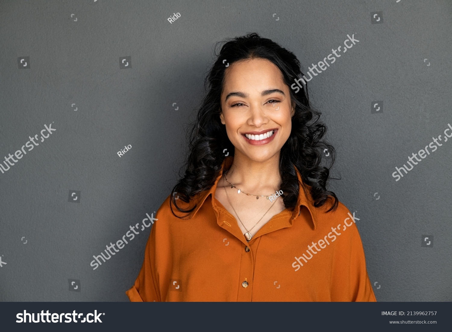Portrait of happy latin young woman isolated on grey wall with copy space. Carefree hispanic woman smiling and looking at camera standing on gray background. Beautiful multiethnic girl laughing. #2139962757