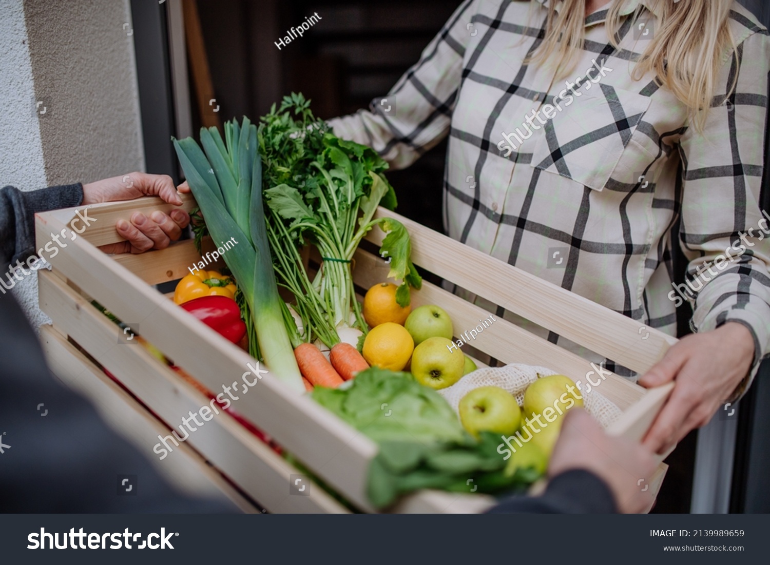 Man holding crate with vegetales and fruit and delivering it to woman standing at doorway. #2139989659