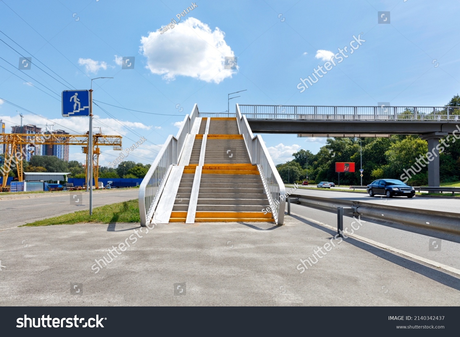 A pedestrian overpass across a busy city highway provides access from a microdistrict under construction to a green city park. ?opy space. #2140342437