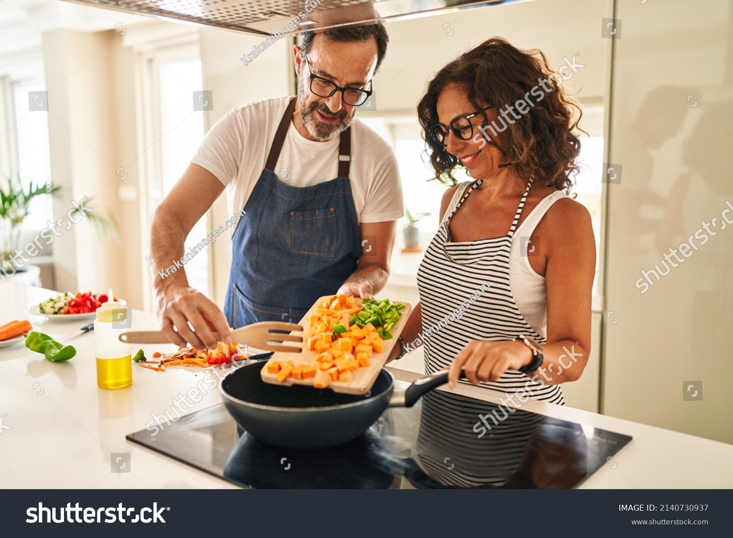 Middle age hispanic couple smiling confident pouring food on frying pan at kitchen #2140730937