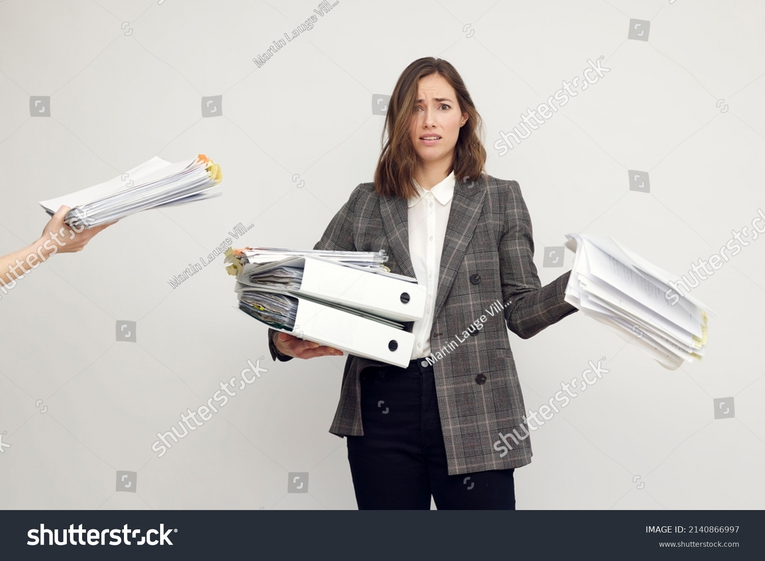 Stressed female worker and business woman holding a pile of paperwork while getting more work to do. Looking frustrated in camera, isolated on white background. Concept: Too much work #2140866997