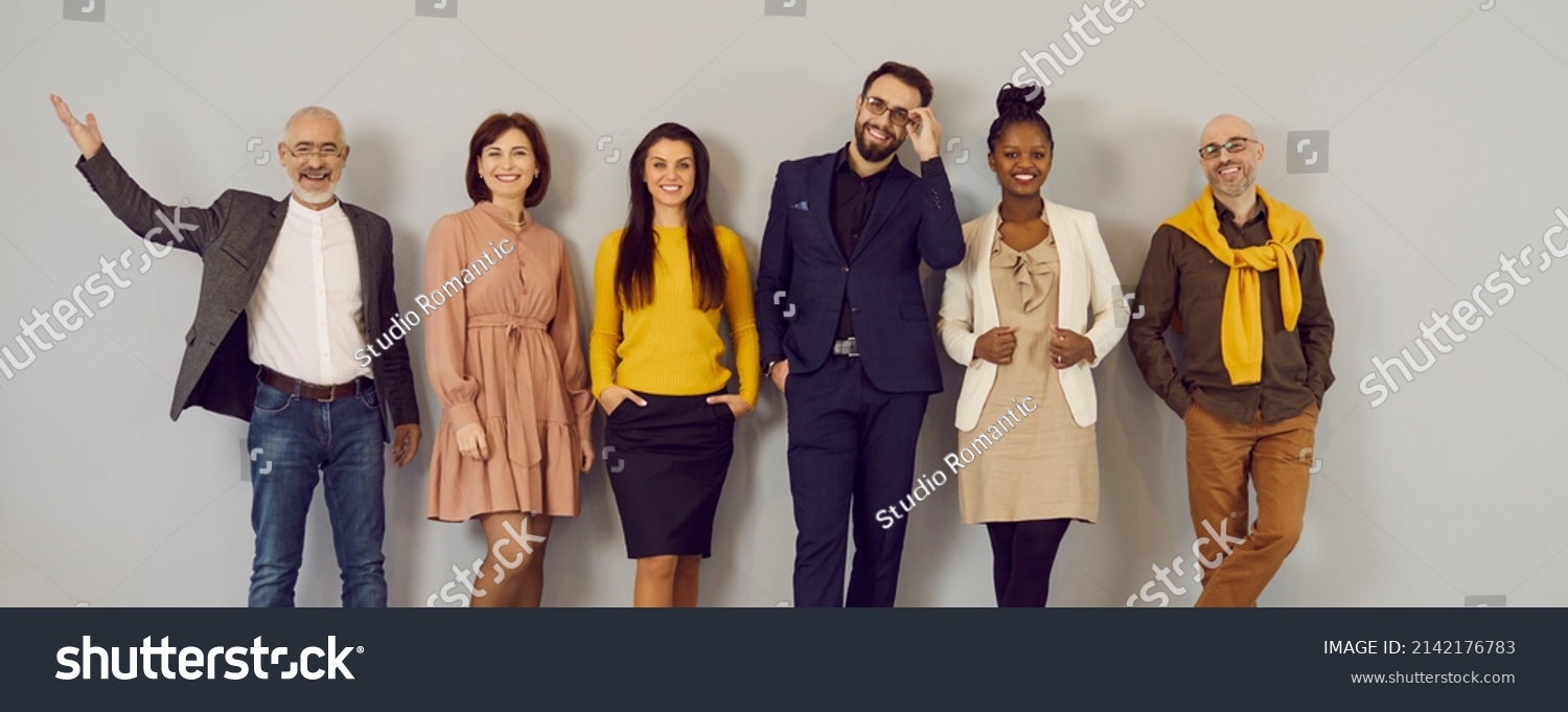 Happy people in clothes suitable for office dress code standing in studio. Mixed race multiethnic group of male and female models in stylish smart casual outfits and glasses posing against grey wall #2142176783