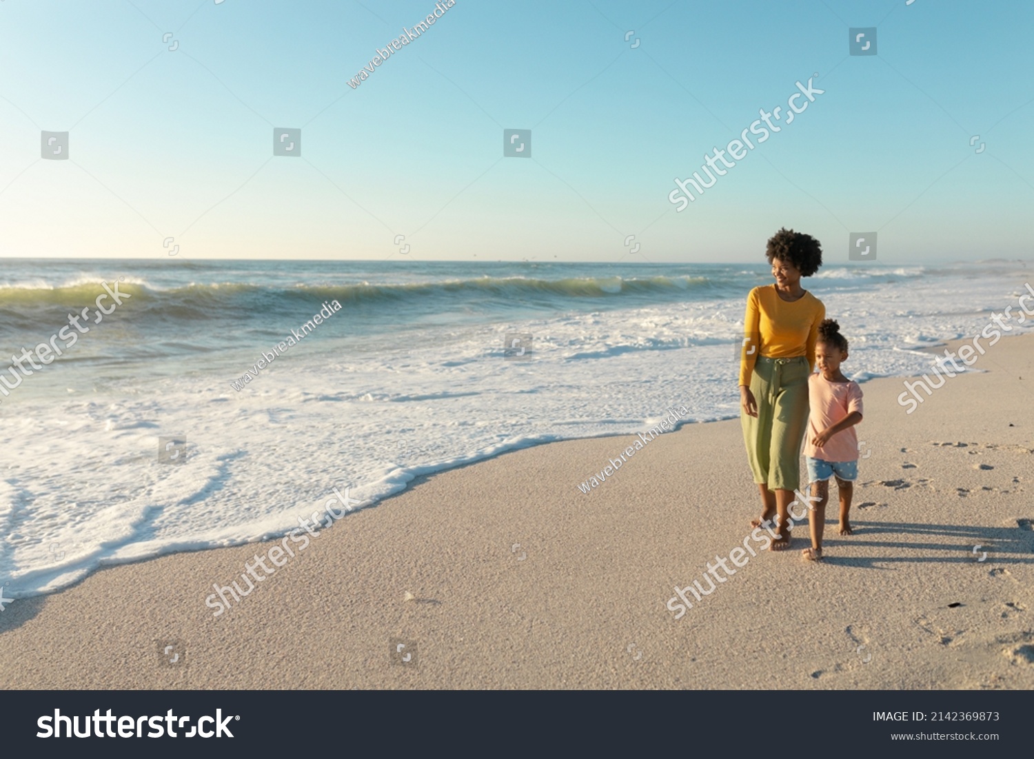 Full length of african american mother and daughter walking on shore at beach with copy space. unaltered, family, lifestyle, togetherness, enjoyment and holiday concept. #2142369873