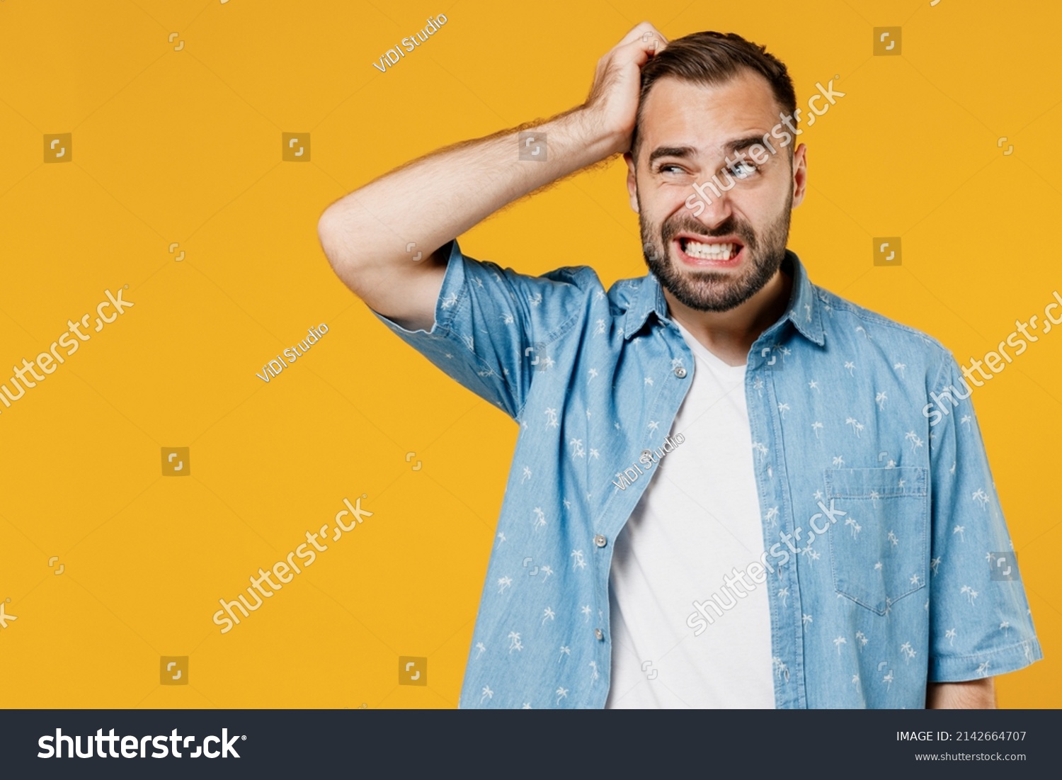 Young puzzled embarrassed bewildered caucasian man 20s wearing blue shirt white t-shirt scratch head look aside say oops isolated on plain yellow background studio portrait. People lifestyle concept #2142664707
