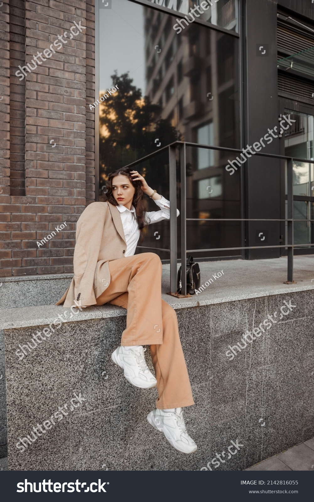  Tall stylish girl with oversized jacket posing near the railing and steps on the city background #2142816055
