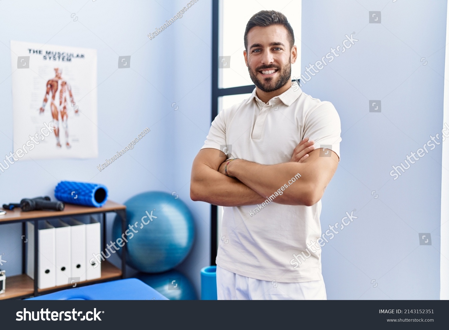 Young hispanic man wearing physiotherapist uniform standing with arms crossed gesture at clinic #2143152351