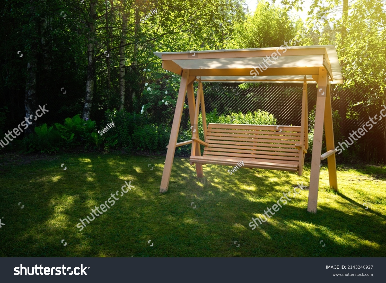 Wooden summer swing on the green grass in the garden. Garden decoration. Landscape design.Summer vacation in the country. #2143240927