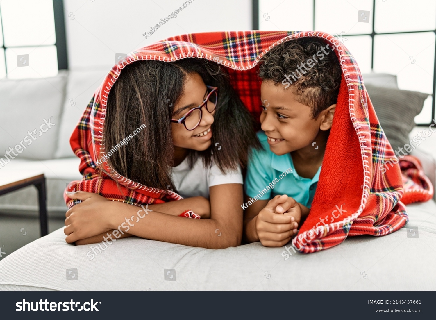 Brother and sister covering with blanket lying on sofa at home #2143437661