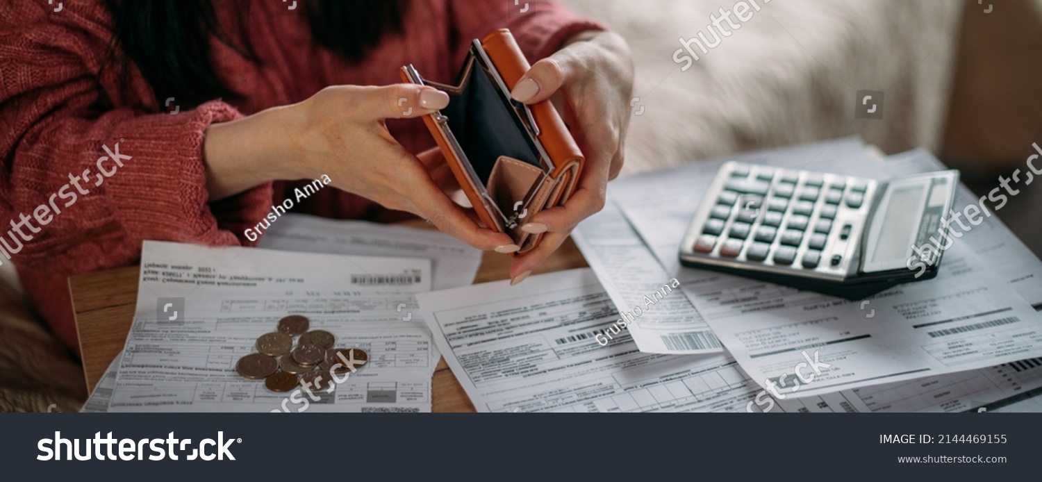 Close-up of woman's hands with empty wallet and utility bills. The concept of rising prices for heating, gas, electricity. Many utility bills, coins and hands in a warm sweater holding an open wallet #2144469155