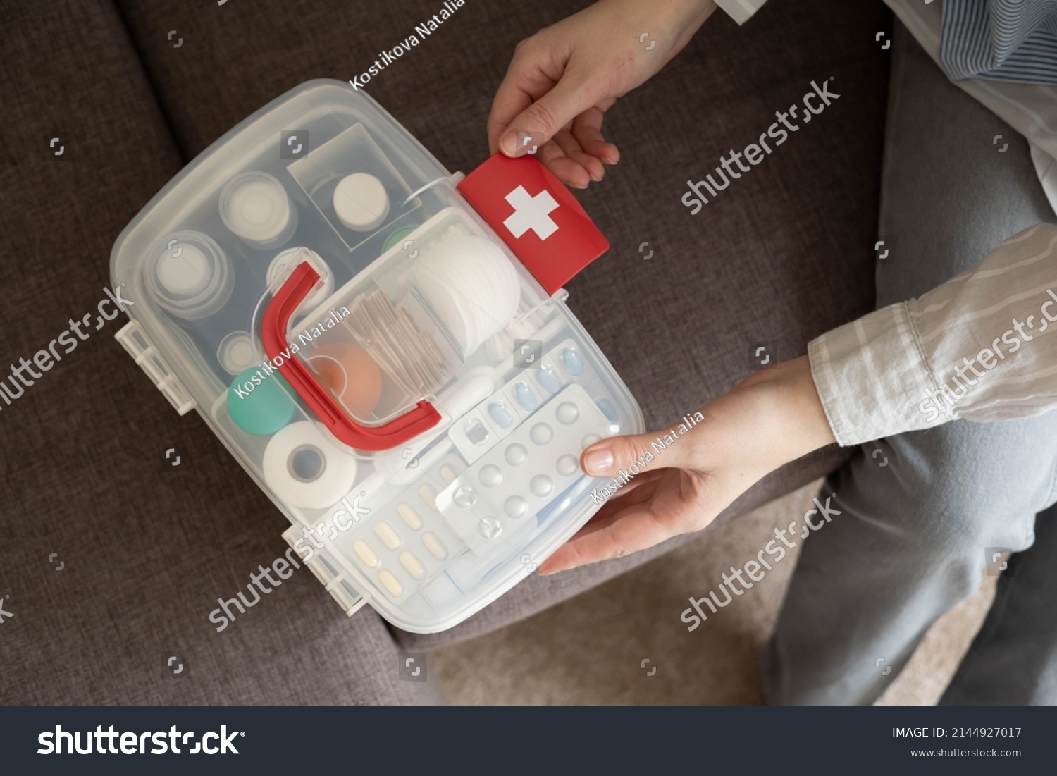 Closeup female hand neatly placing medicament at domestic first aid kit top view. Storage organization in transparent plastic box drug, pill, syringe, bandage. Fast health help safety emergency supply #2144927017