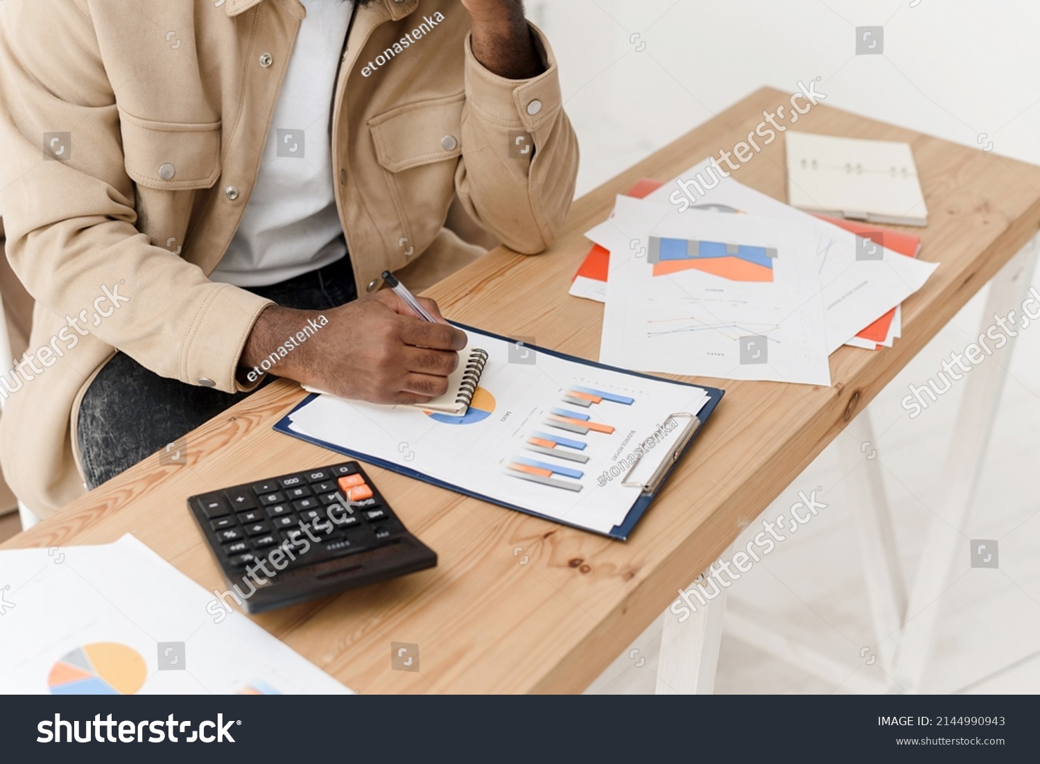 Close-up of an African American man calculating with a calculator, managing household finances, or keeping company financial records at home. Black man making calculations on a calculator, paying #2144990943