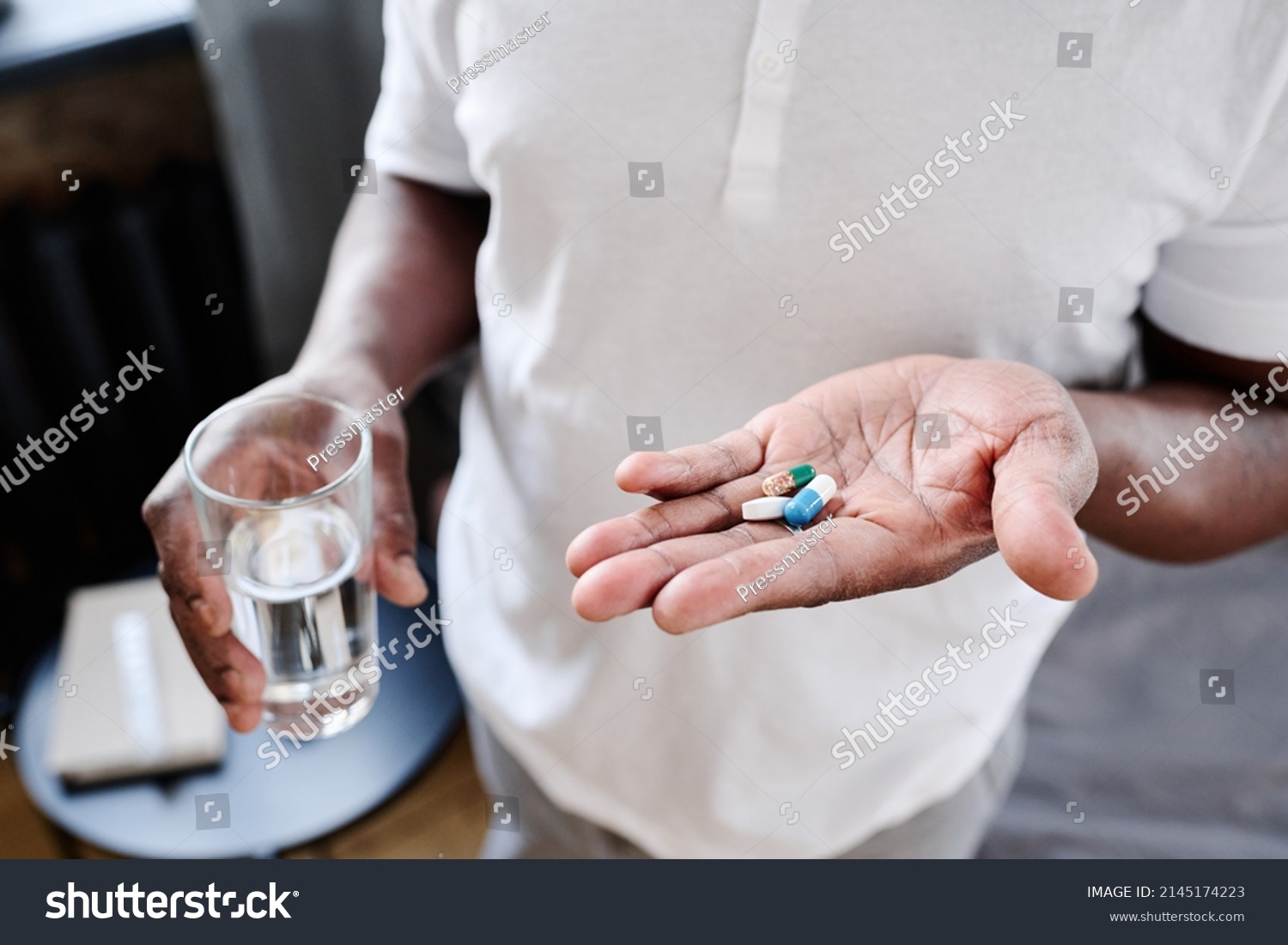 African American senior man with glass of water and three pills on hand going to take medicaments prescribed by his physician #2145174223