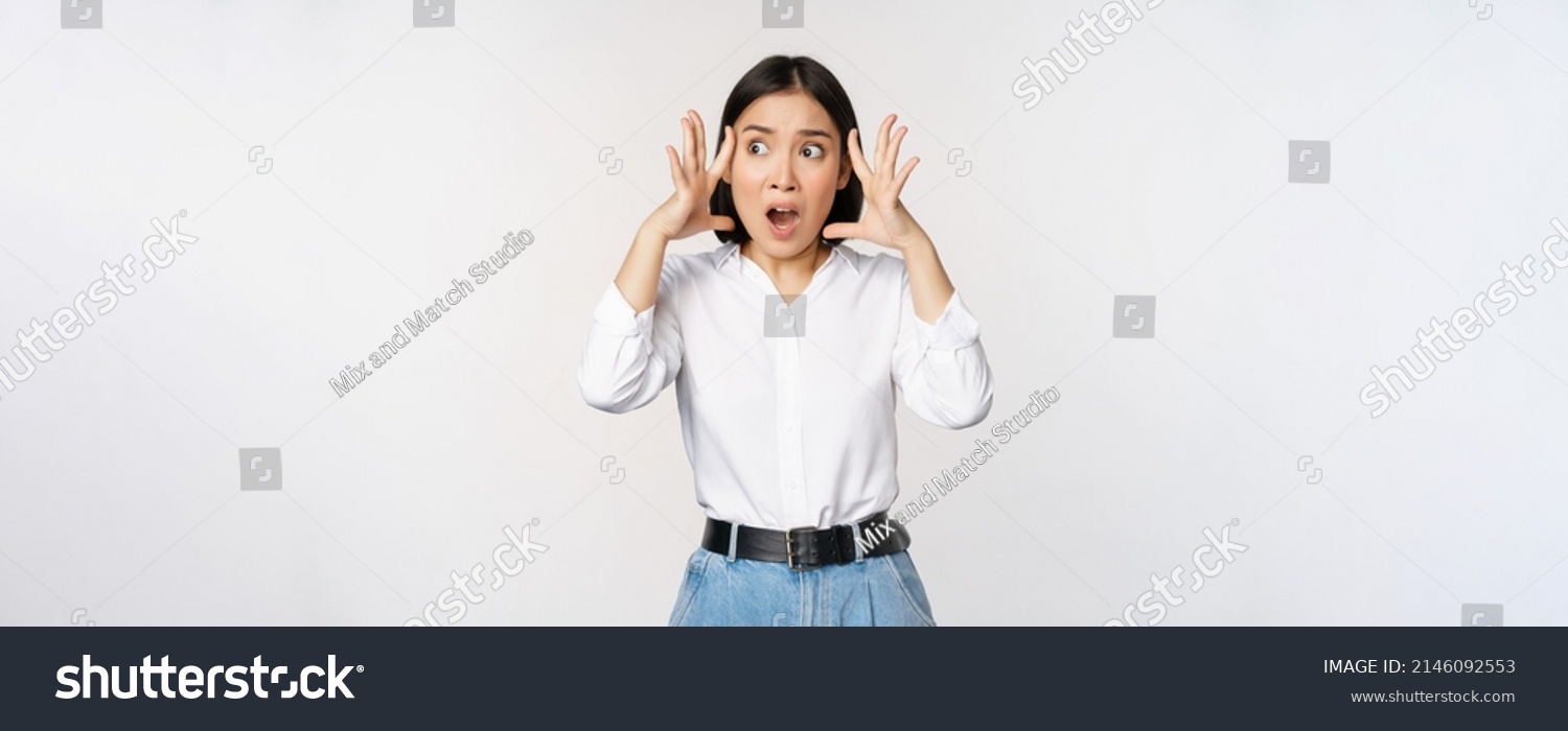 Image of shocked anxious asian woman in panic, holding hands on head and worrying, standing frustrated and scared against white background #2146092553