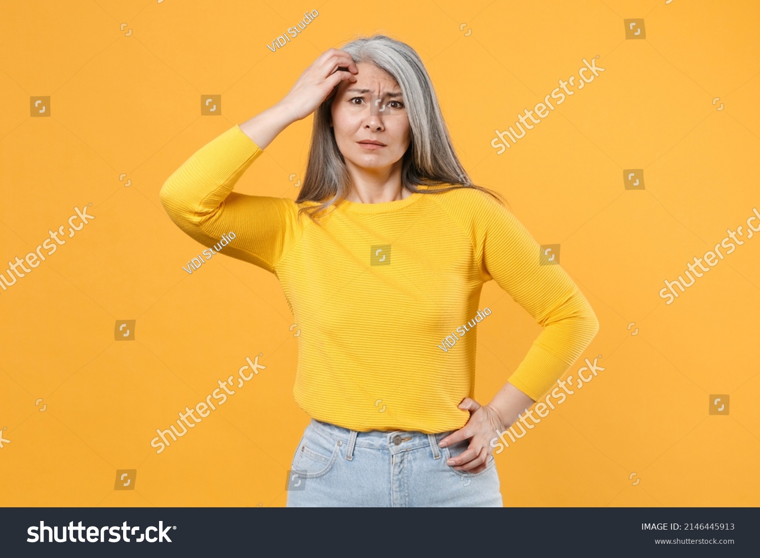 Preoccupied puzzled worried concerned perplexed gray-haired asian woman wearing casual clothes standing put hand on head looking camera isolated on bright yellow colour background, studio portrait #2146445913