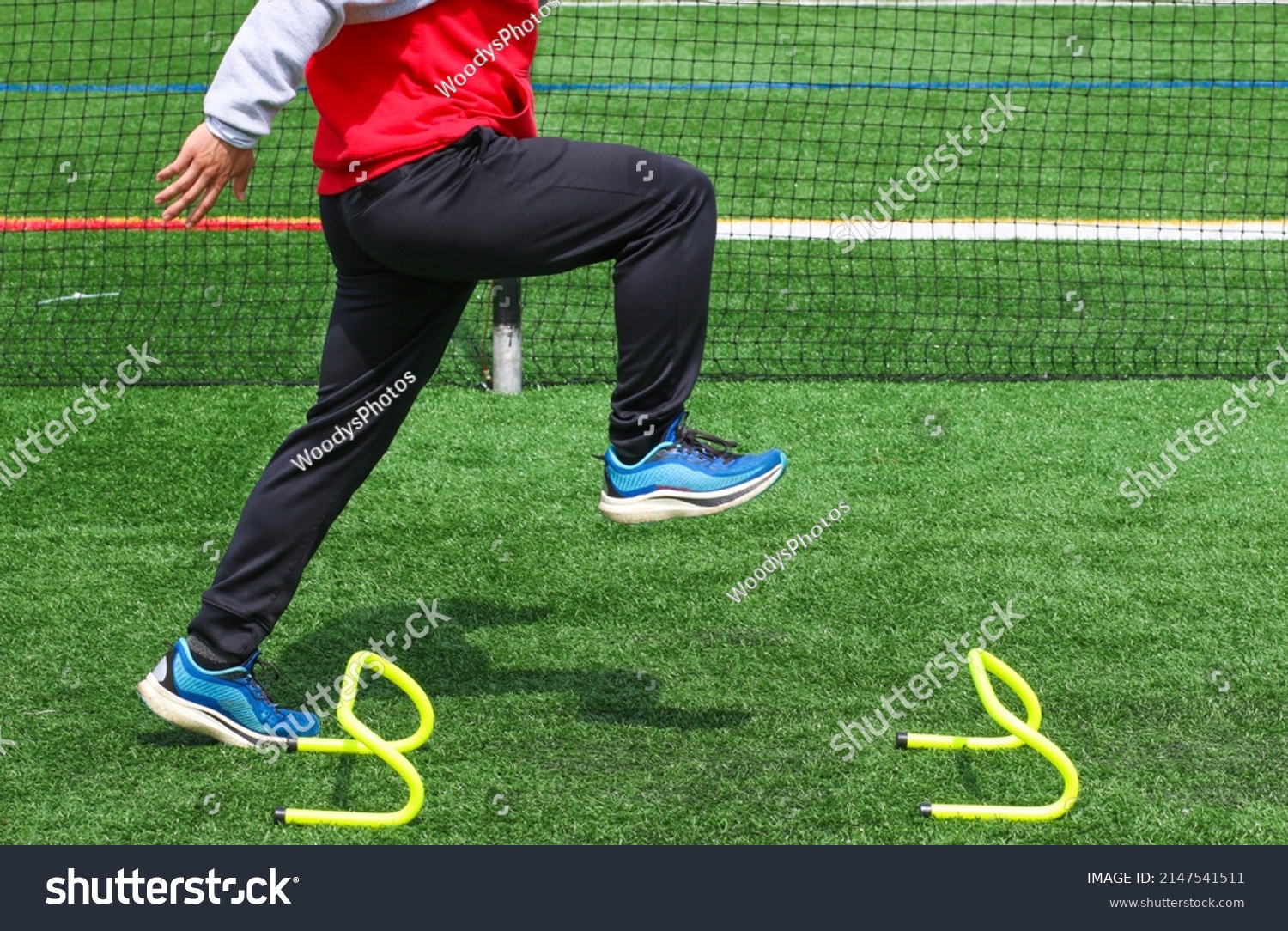Side view of a high school track runner standining in the track A position over a small yellow hurdle doing sports training drills. #2147541511