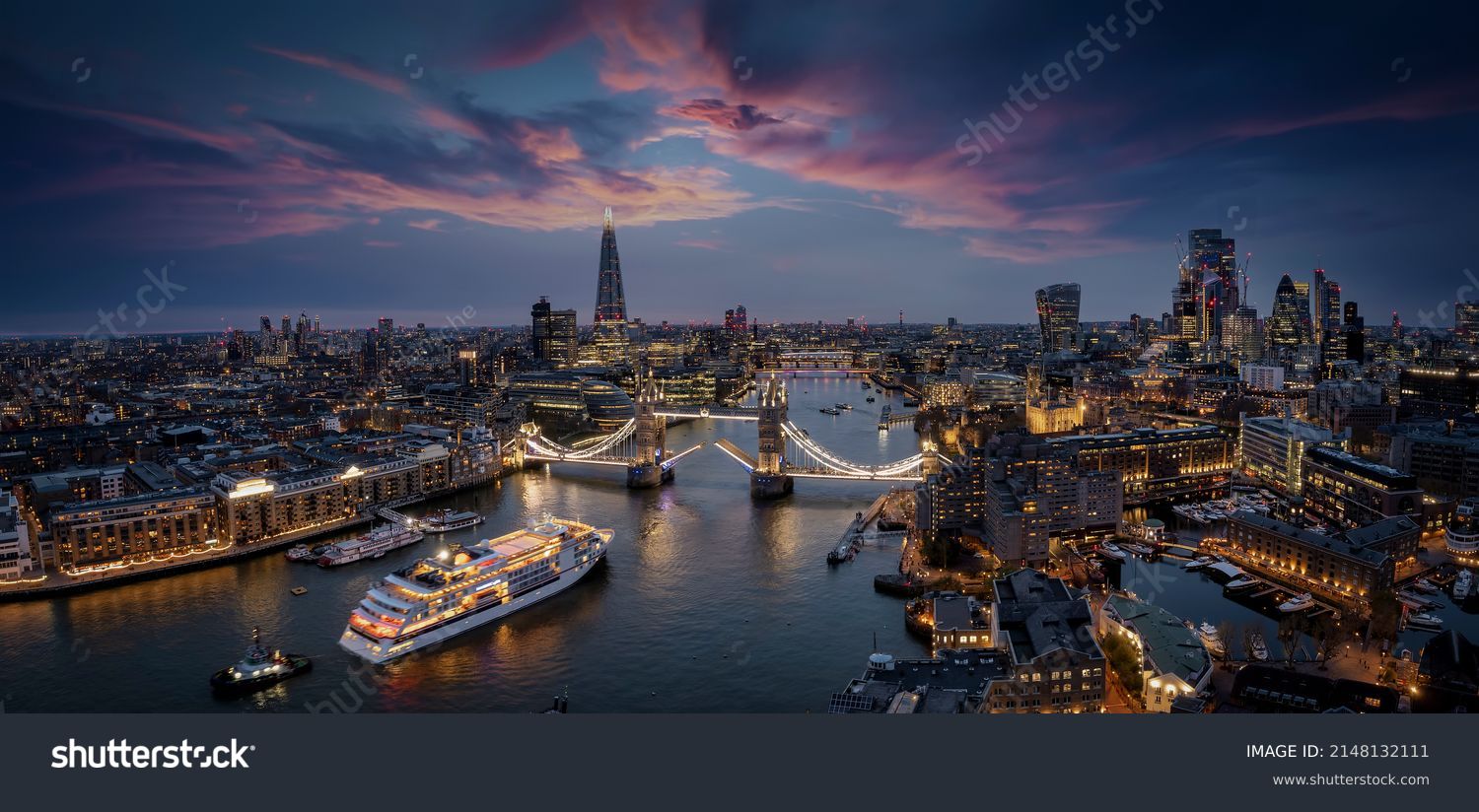 Panoramic, aerial view of the skyline of London with a motion blurred cruise ship passing under the lifted Tower Bridge during dusk, England #2148132111