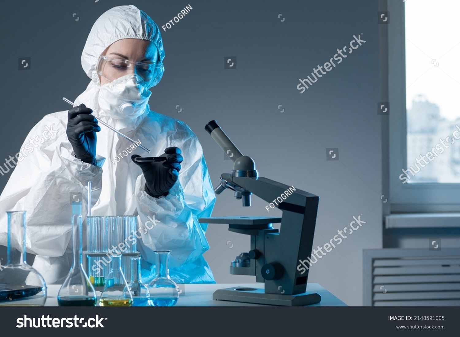 Dispersal of viruses. Member of Institute of Virology. Laboratory research of viruses. Doctor is engaged in dispersal of viruses. Medic in chemical protection suit. Microscope and tube in doctor hand #2148591005