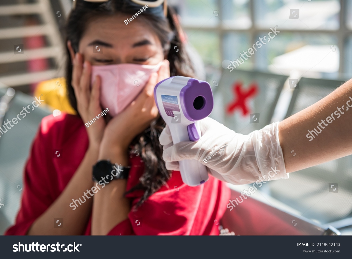 Shocked traveler with mask see high temperature result from Medical infrared thermometer on officer hand. woman in airport terminal disallow to departure due to covid-19 omicron virus. #2149042143