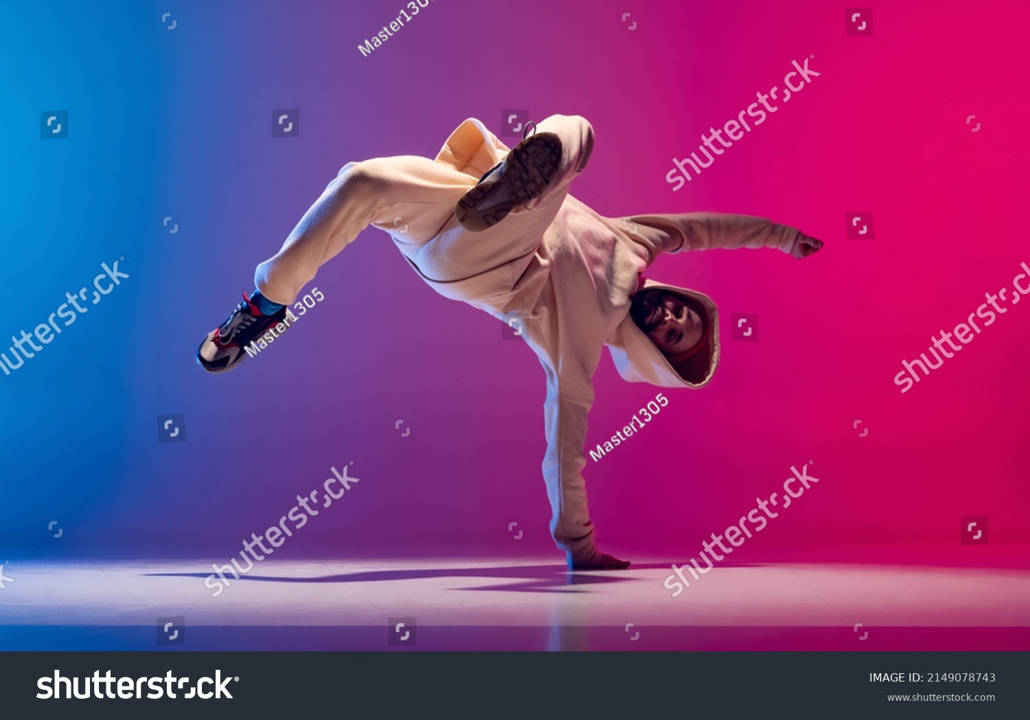 Hand stand. Studio shot of young flexible sportive man dancing breakdance in white outfit on gradient pink blue background. Concept of action, art, beauty, sport, youth. Dancer shows breakdance #2149078743