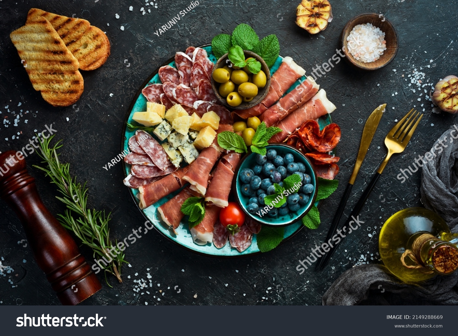 Italian snacks. Plate with cheese and ham, prosciutto, jamon salami, and snacks. On a black stone background. #2149288669
