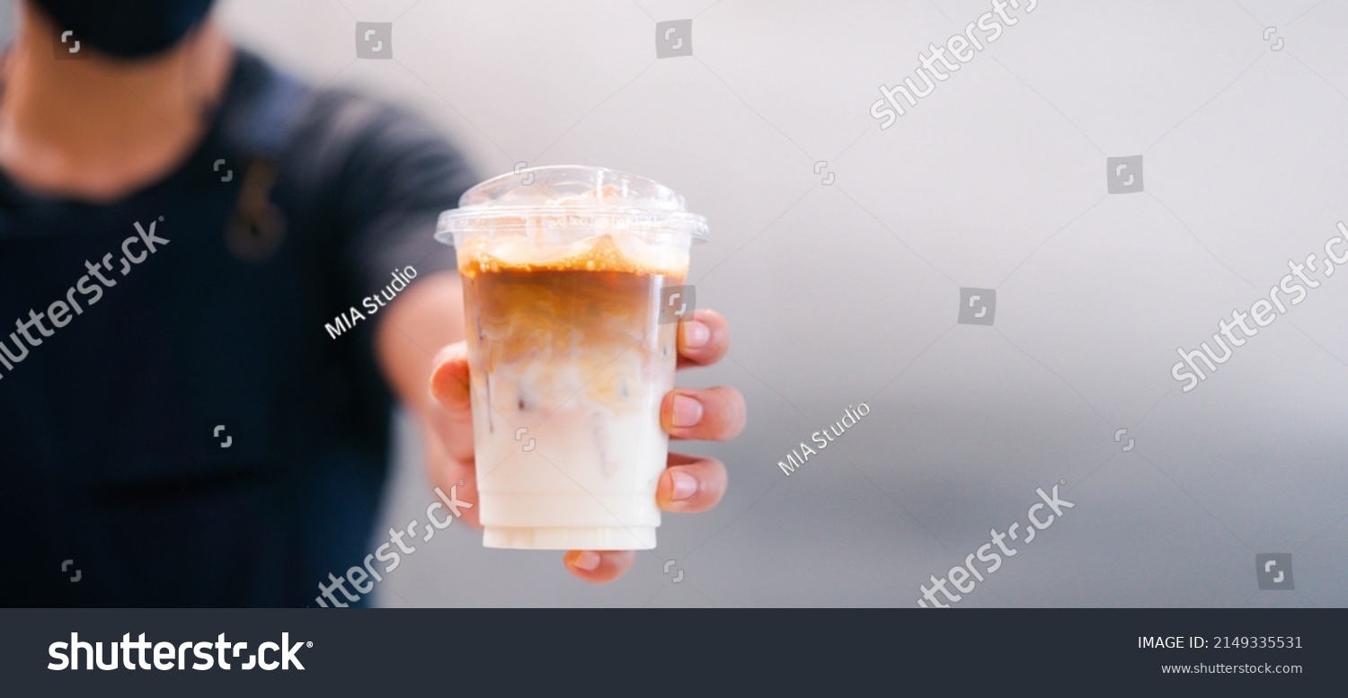 Cold brewed iced latte coffee, Ice coffee latte cup in a plastic glass on. barista hand in coffee cafe.banner background.Cold brew coffee ads.Latte with milk caffeine.plastic ice cup.Arabica roasted. #2149335531