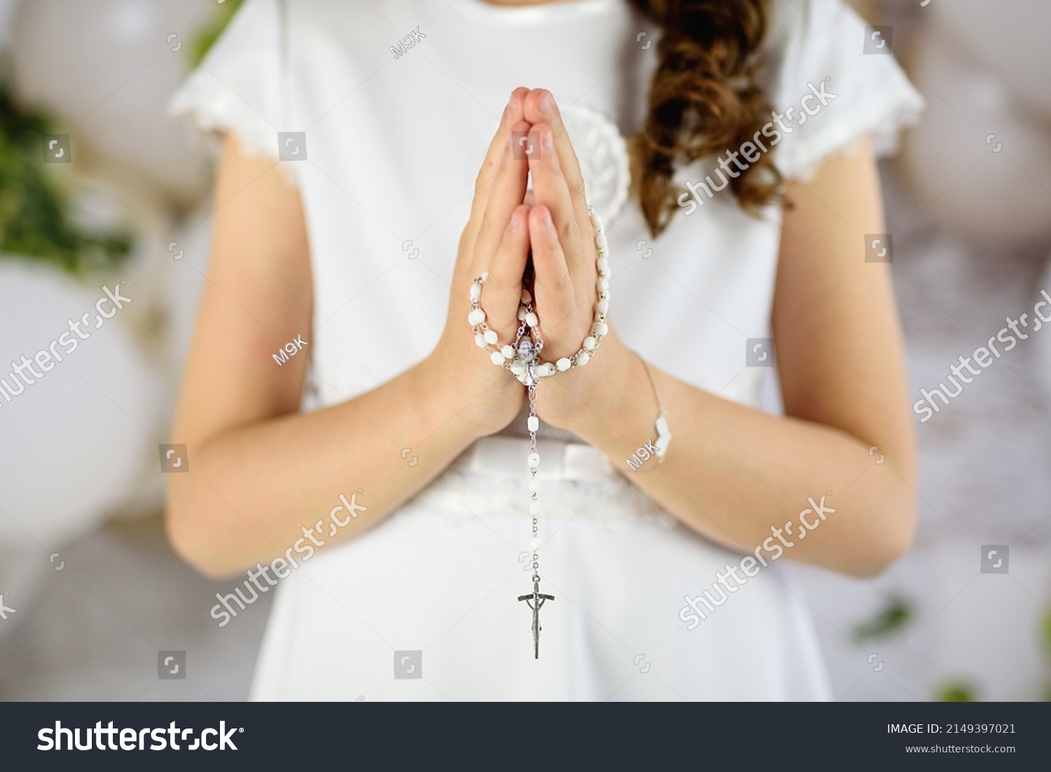 
Hands of the First Communion girl folded in prayer. First Holy Communion. A girl in a white communion dress after receiving her First Holy Communion  #2149397021