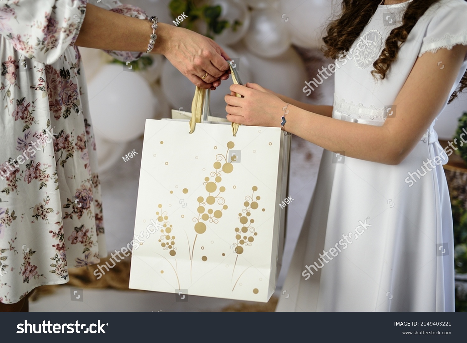 A gift from godparents for the first holy communion. A woman giving the girl a First Communion gift. First Communion gifts in decorative bags. #2149403221