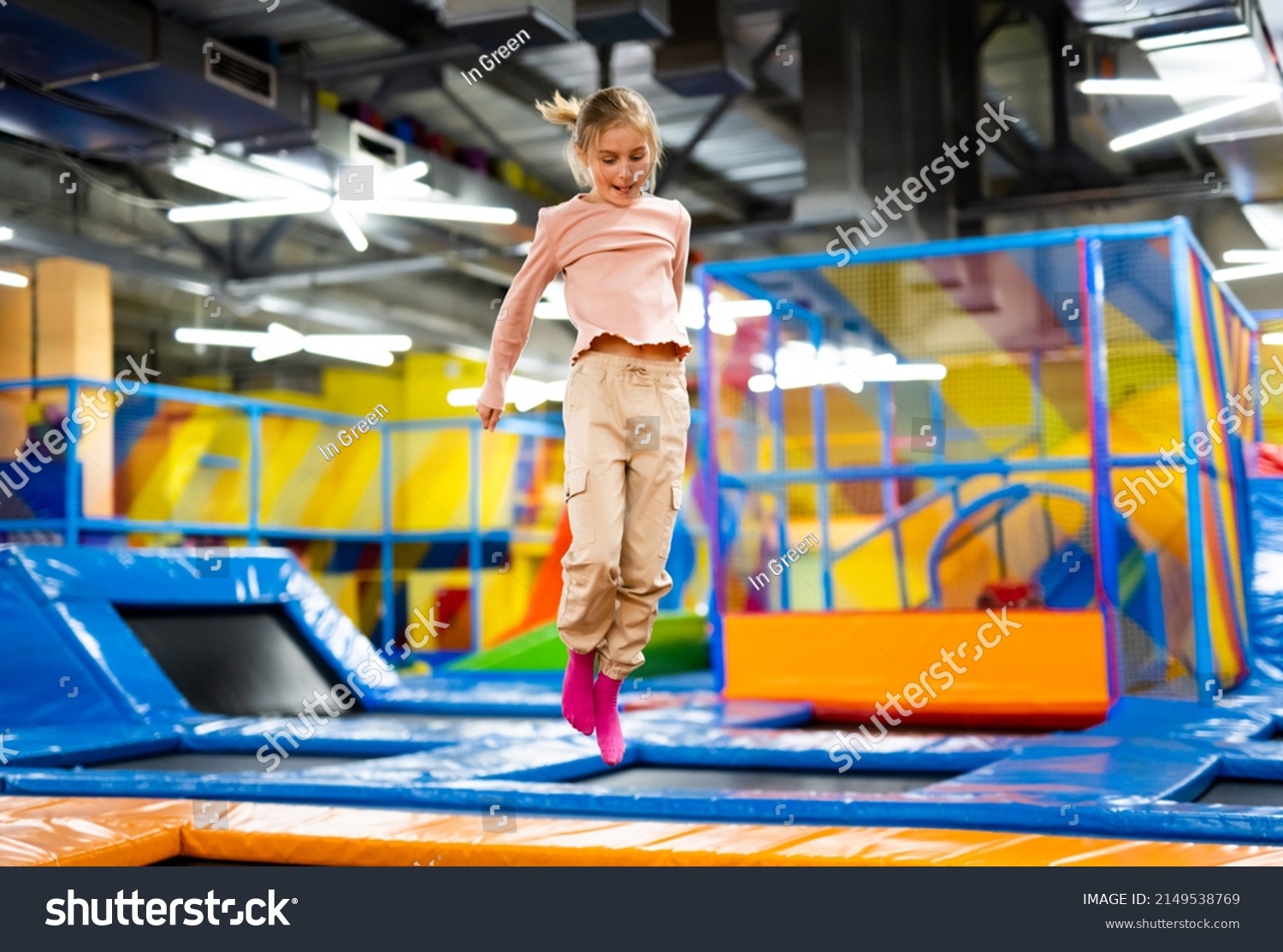 Pretty girl kid jumping on colorful trampoline at playground park and smiling. Caucasian preteen child during active entertaiments indoor #2149538769