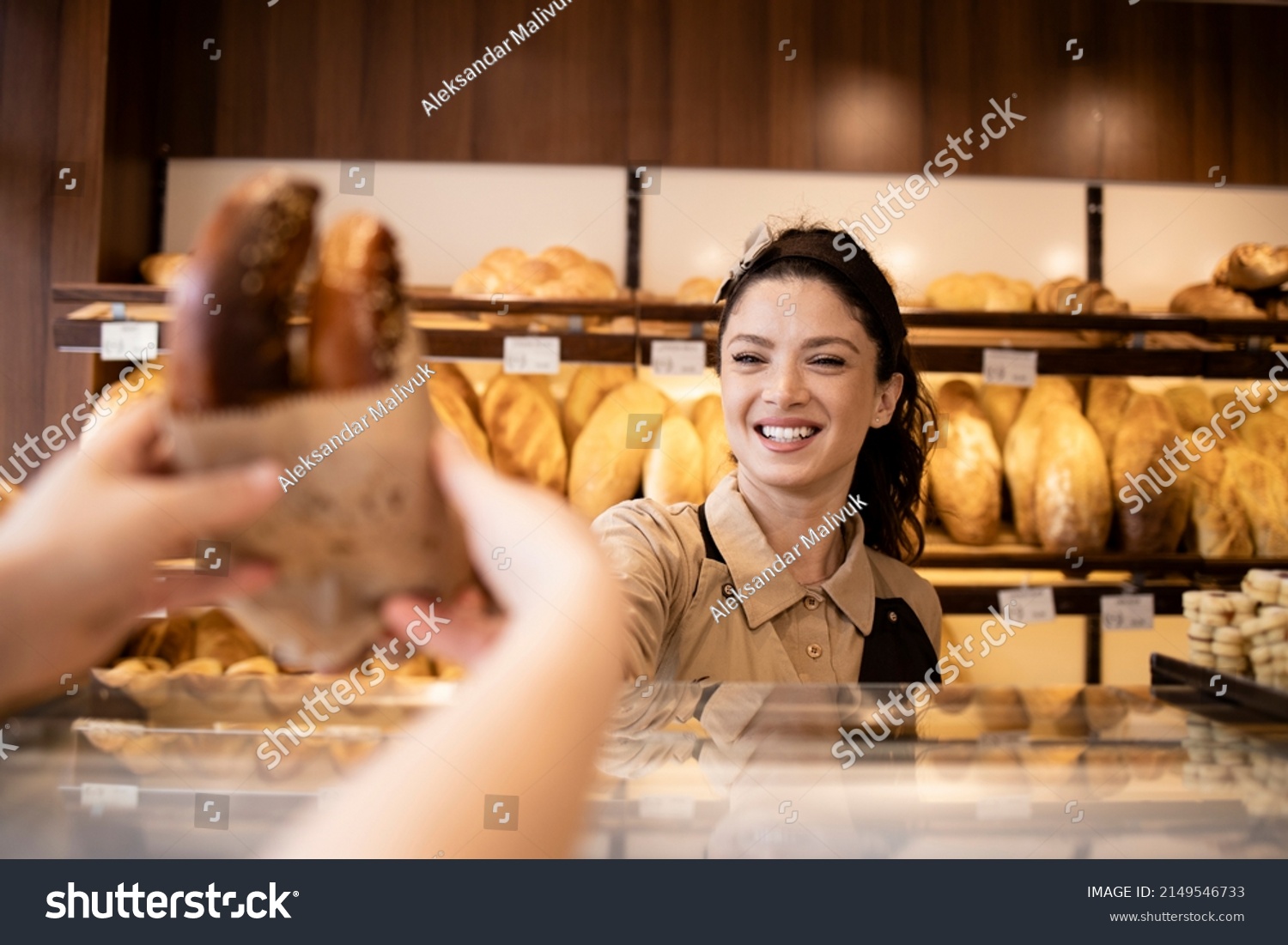 Beautiful smiling bakery worker selling pastry to the customer in bakery shop. #2149546733