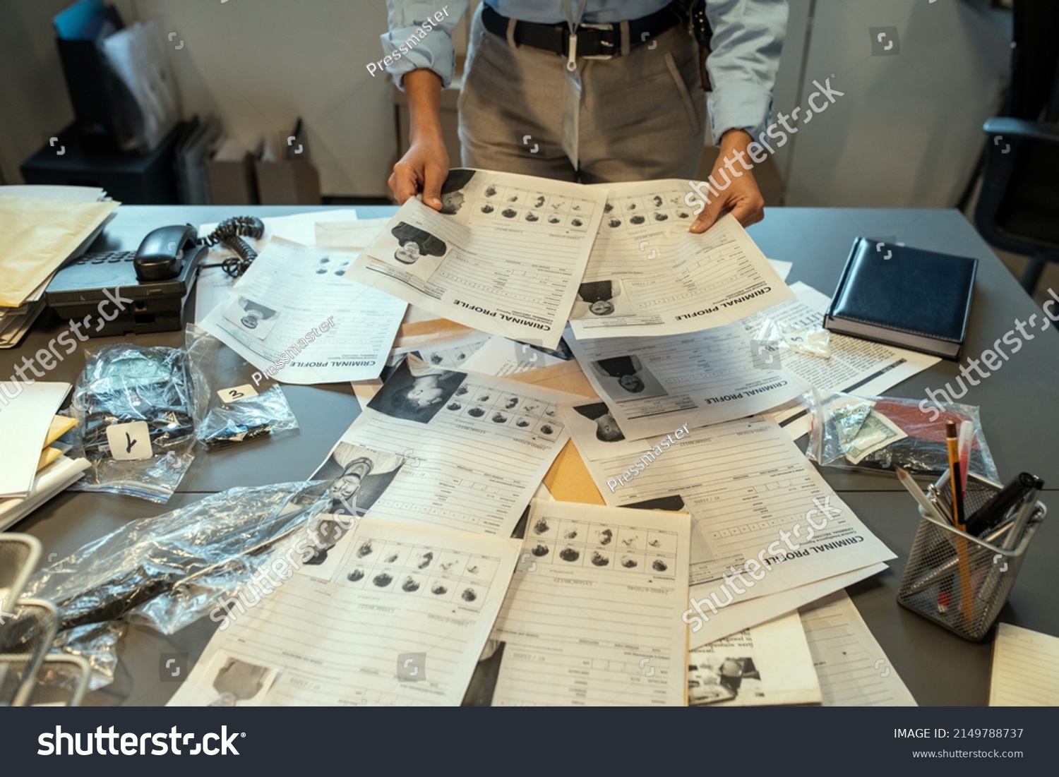 Hands of female investigator holding criminal profiles over desk with documents while learning personal information about suspects #2149788737
