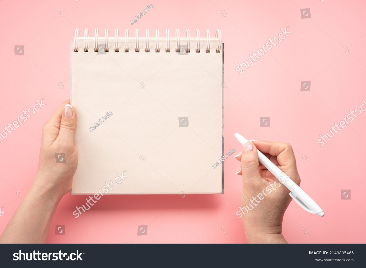 writing in blank notepad on pink background. Mockup notepad. woman hand with pen next to an empty blank notepad. top view of hand holding pen against spiral notepad on pink table, taking notes concept #2149805465