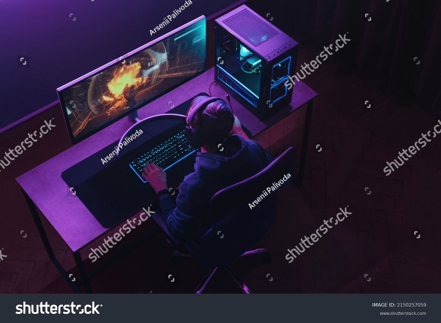 Top view of professional cyber sportsman in headphones playing shooter video game on his powerful gaming PC in dark neon room at night. Pro gamer participates in online esport tournament. Cyber sport #2150257059