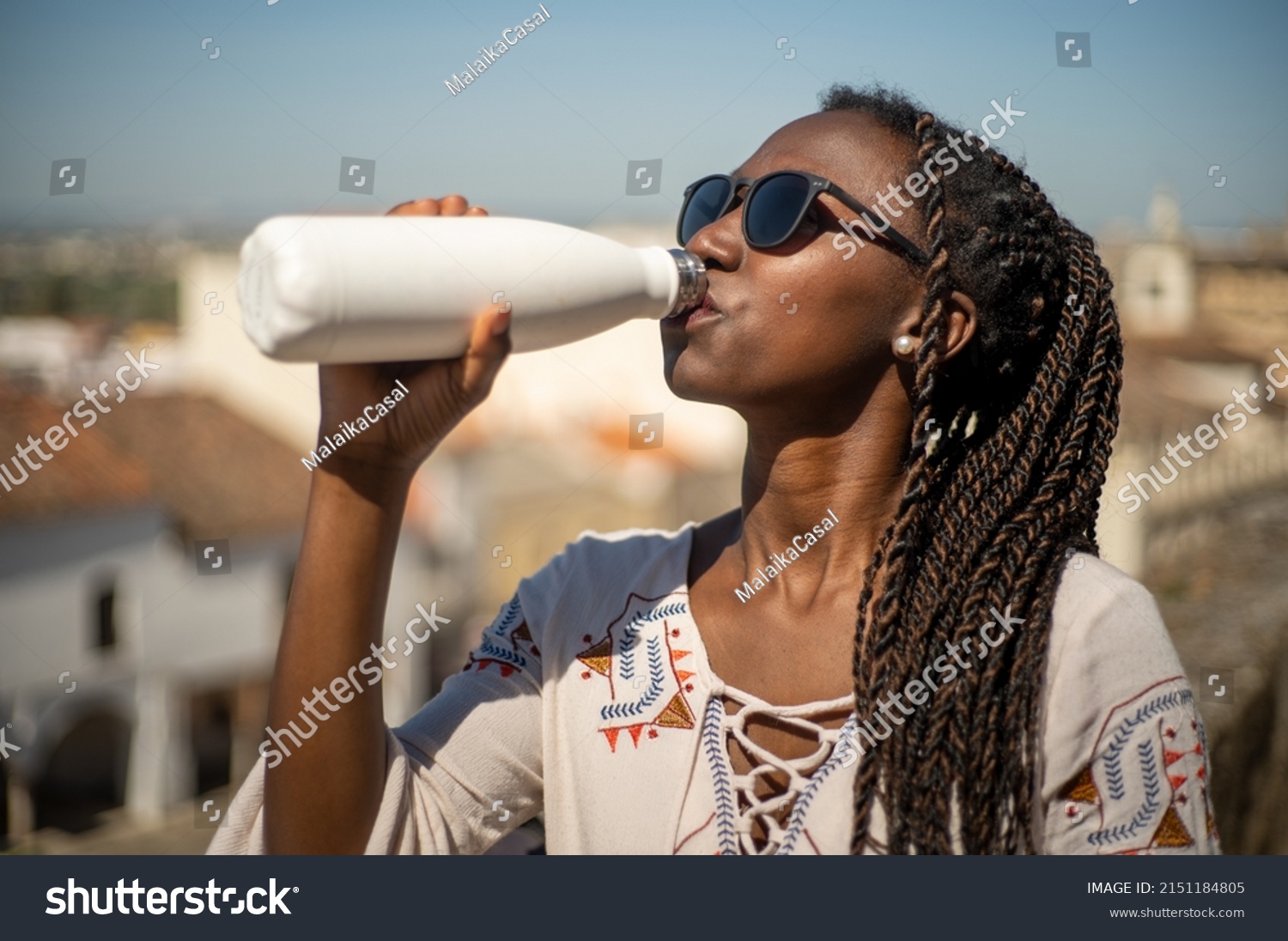 Young woman with sunglasses drinking water from a reusable bottle in a sunny day #2151184805
