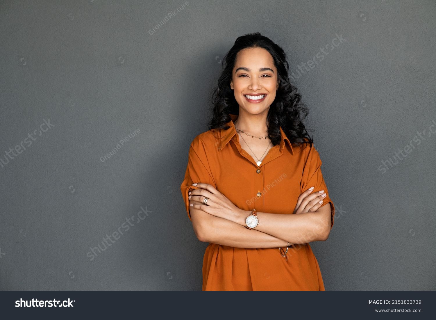 Portrait of a young latin woman with pleasant smile and crossed arms isolated on grey wall with copy space. Beautiful girl with folded arms looking at camera against grey wall. Cheerful hispanic woman #2151833739