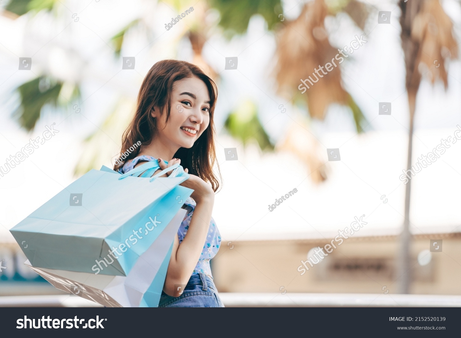 Wellbeing single lifestyle on holidays. Happy young adult southeast asian woman with shopping bags on day. Wear blue shirt with long hair. #2152520139
