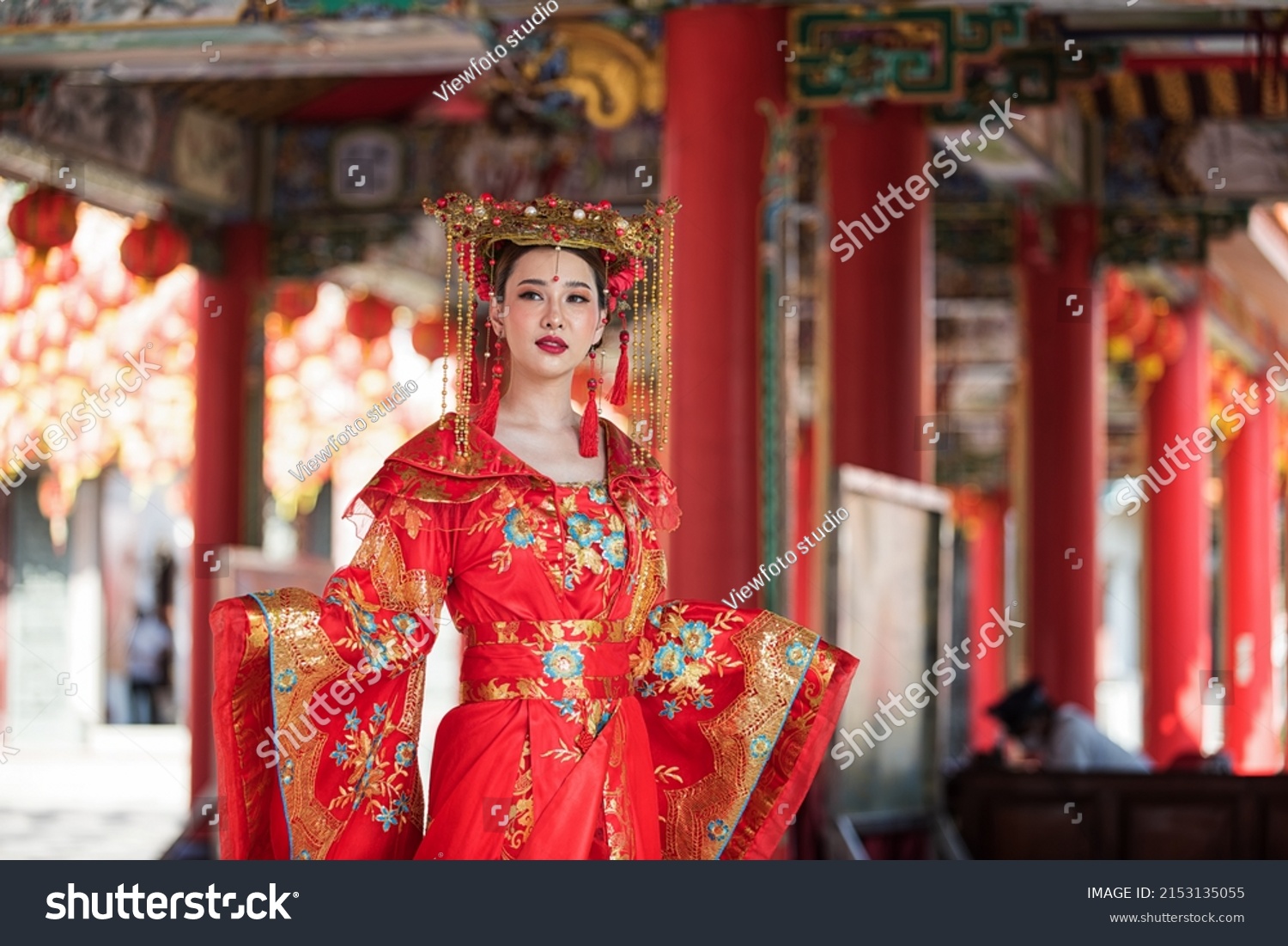 portrait of a woman. person in traditional costume. woman in traditional costume. Beautiful young woman in a bright red dress and a crown of Chinese Queen posing against the ancient door.  #2153135055